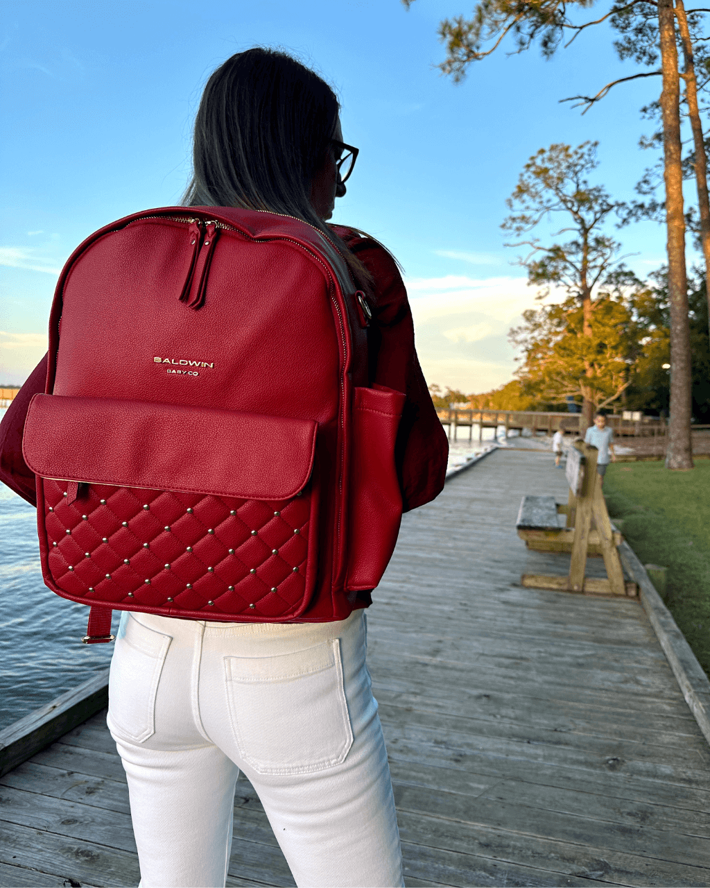 Crimson diaper backpack worn on the back, showing its quilted front pocket and side bottle pocket.