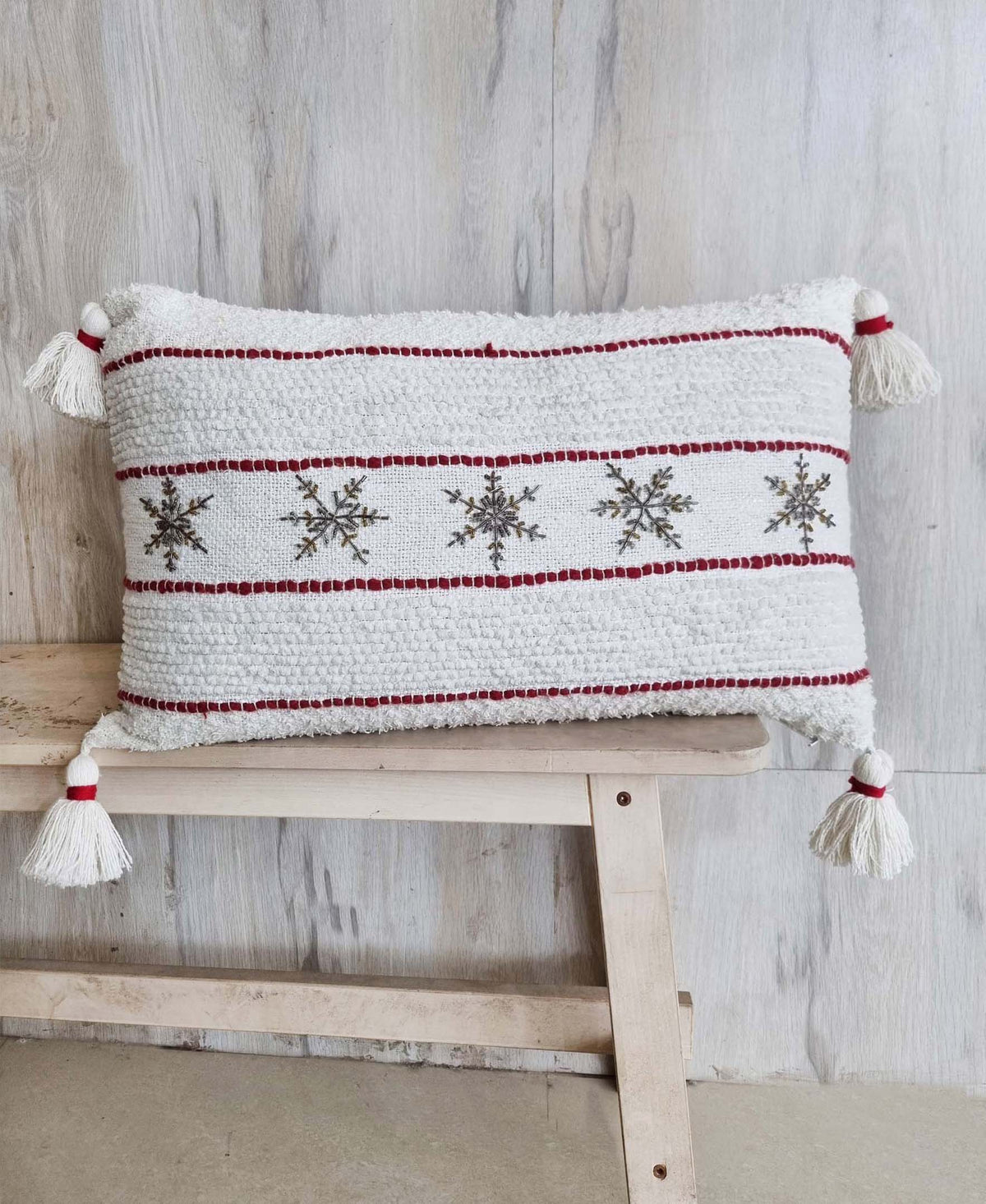 Decorative Christmas pillow with red horizontal stripes, snowflake motifs, and tassel trim