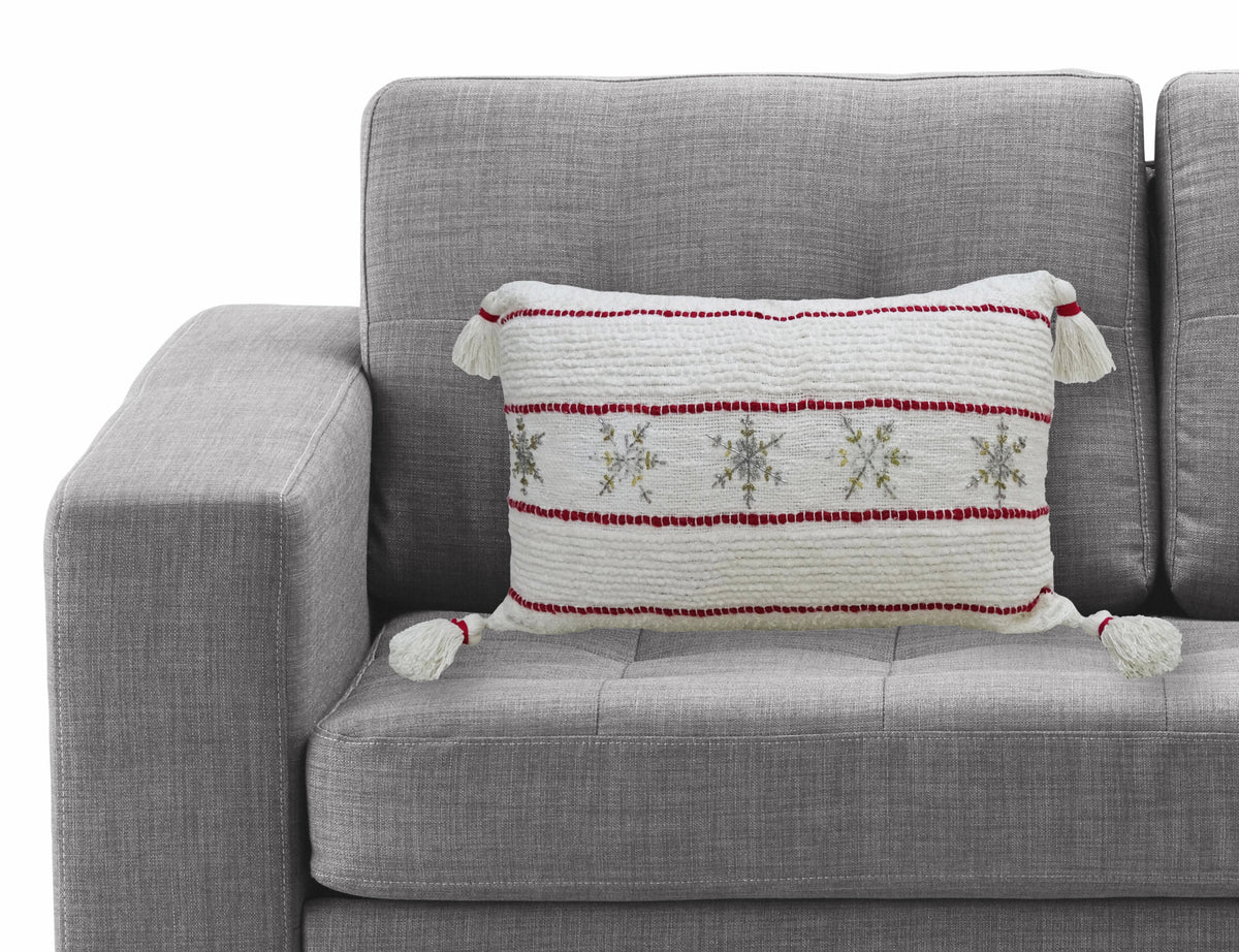 Decorative Christmas pillow on a gray sofa, featuring red-striped snowflake design and tassels