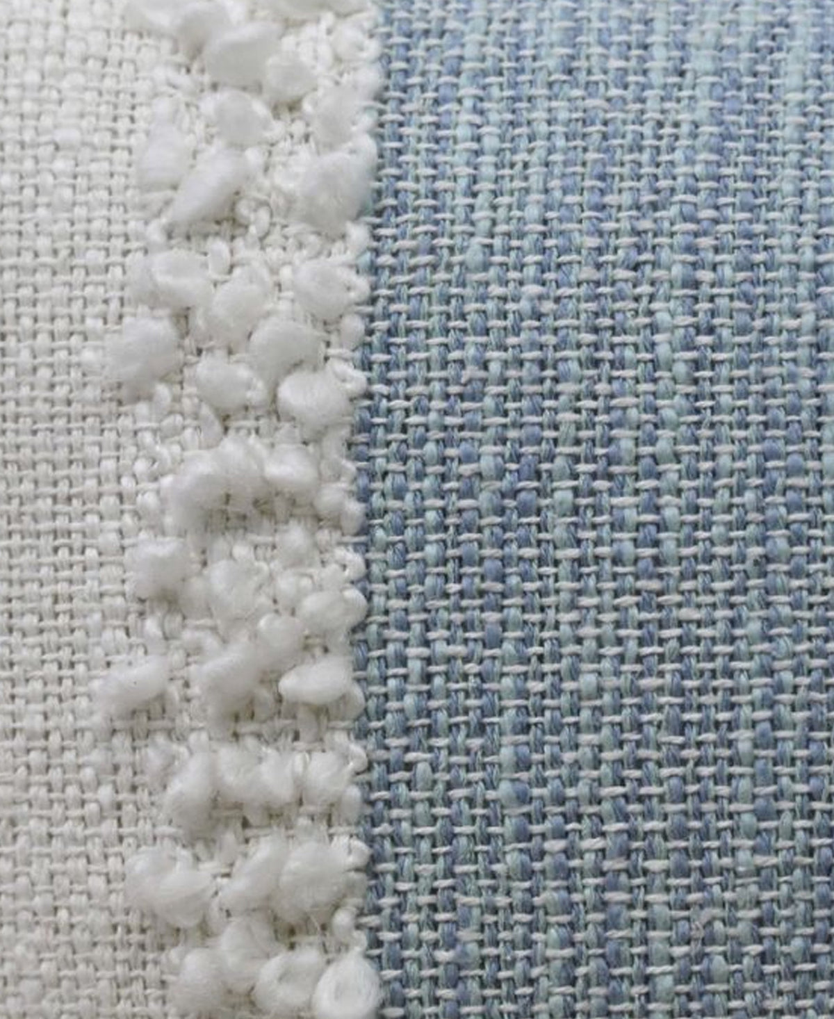 Close-up of cream and light blue woven pillow fabric with pom-pom textured border