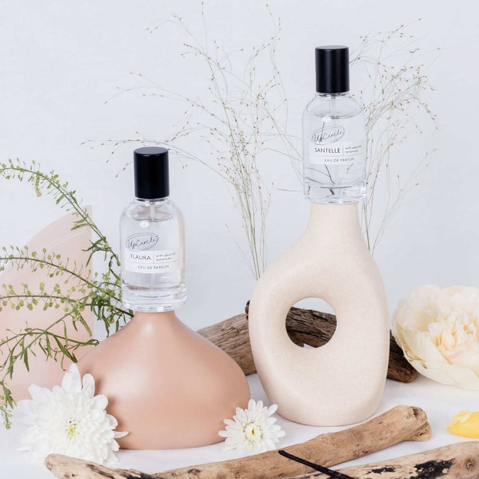 Eau de parfum set bottles with black caps beside a carved stone and flowers.