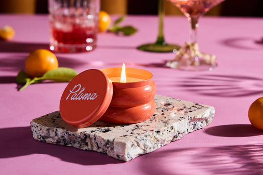 Rewined Paloma candle in a coral glass jar with a matching lid and visible flame