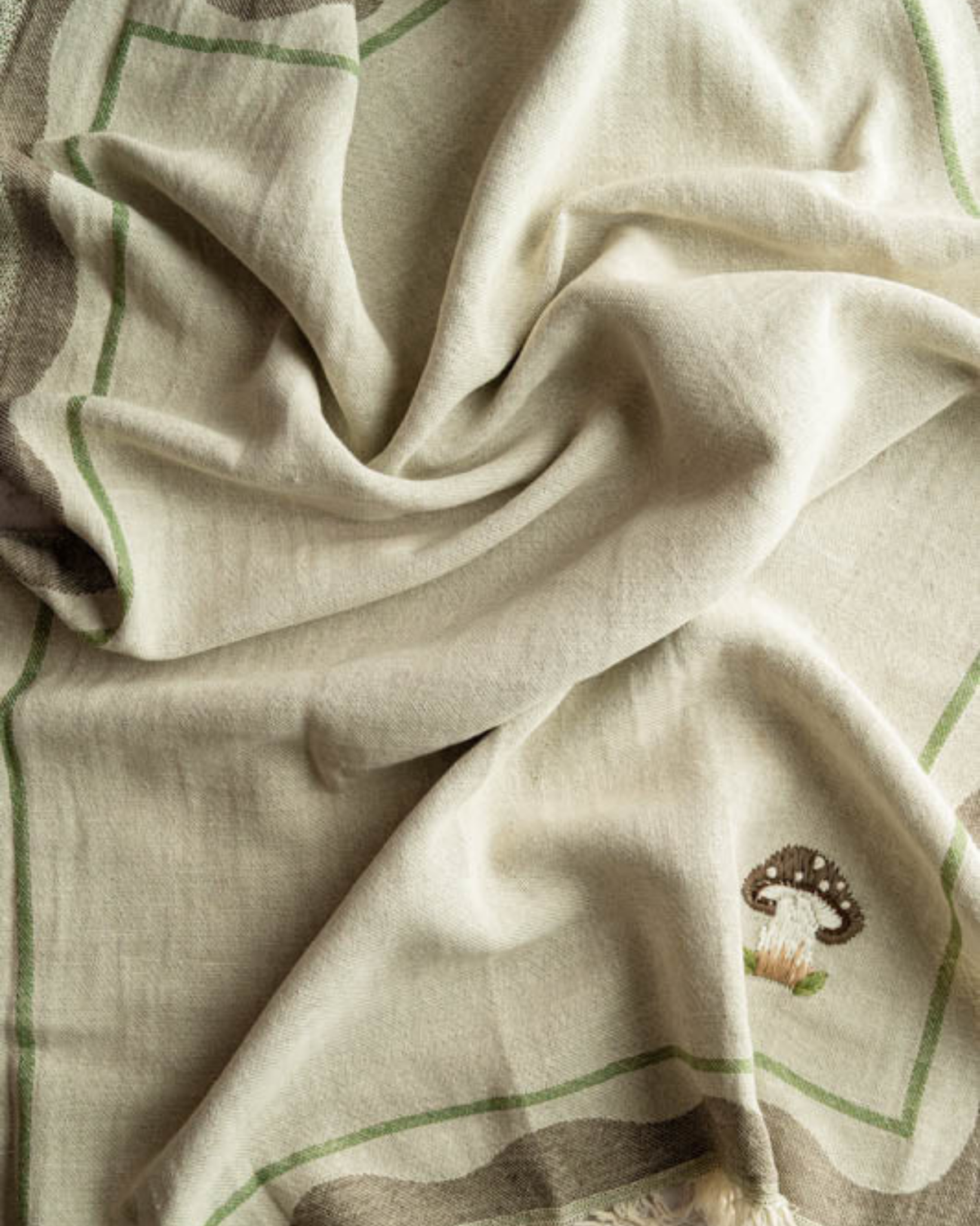 Draped tea towel fabric with green stripe border and partial mushroom embroidery