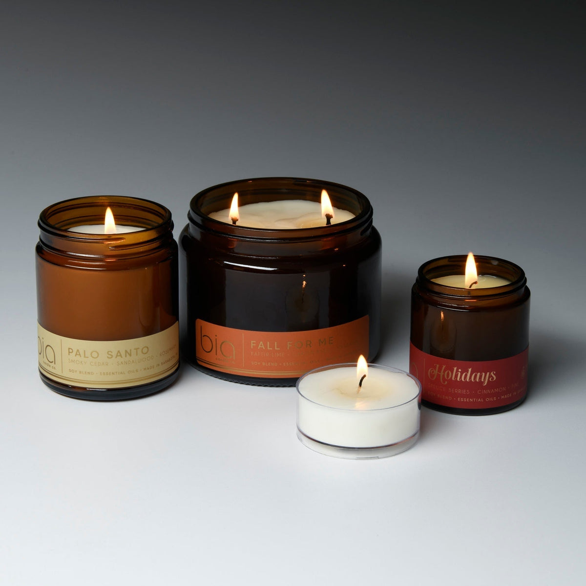 Amber glass soy candle with three wicks, lit, on dark and white candle holders