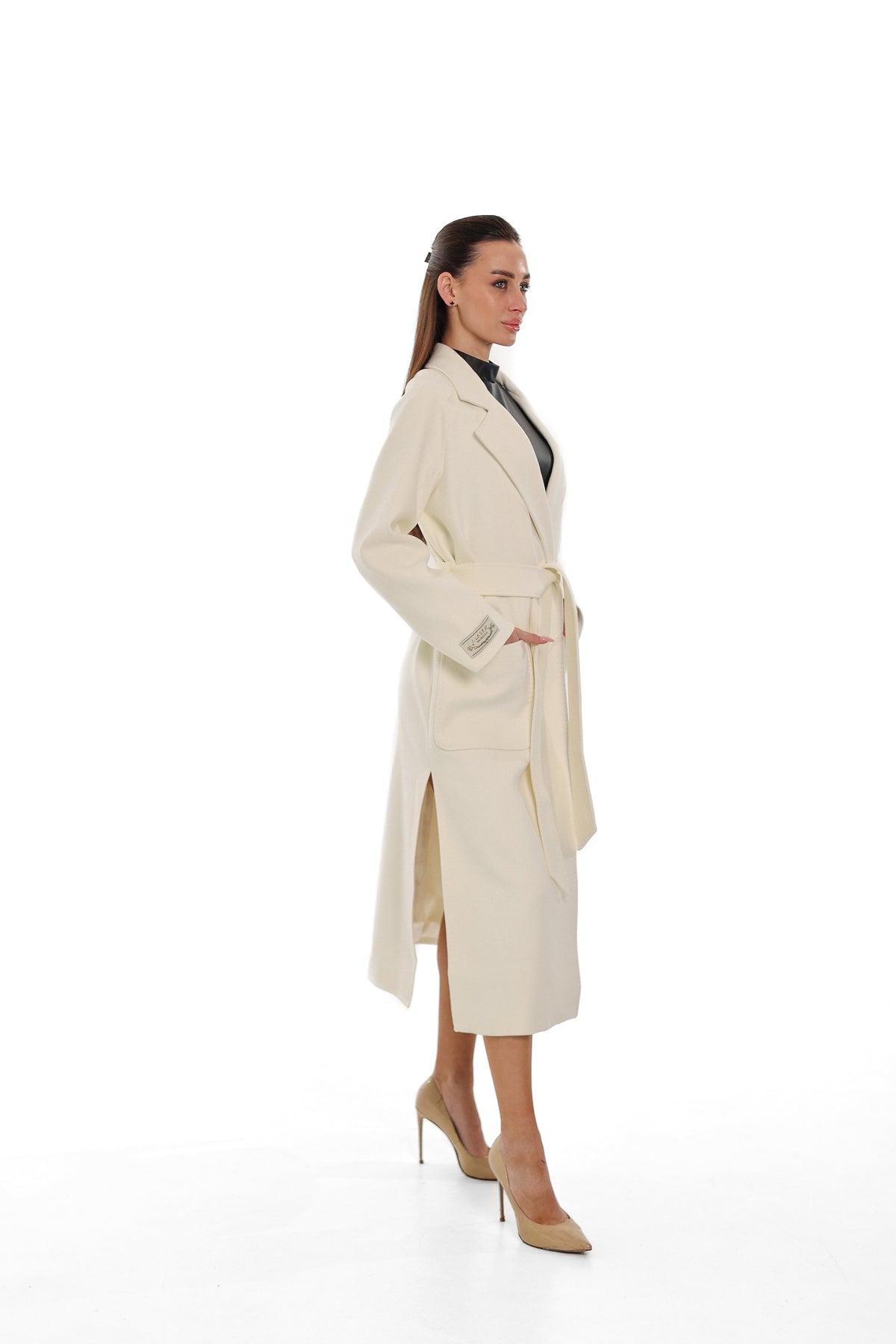 Side view of the ivory overcoat with a belted waist and long hem