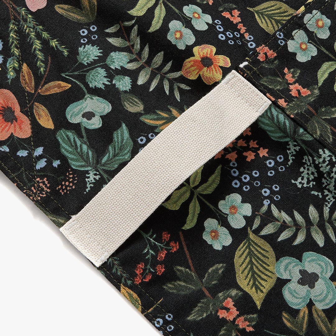 Black floral apron with beige strap and angled stitched seam detail