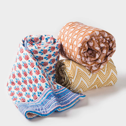 Cotton throw set with blue leaf print, orange-brown patterned throw, and chevron stripe fold