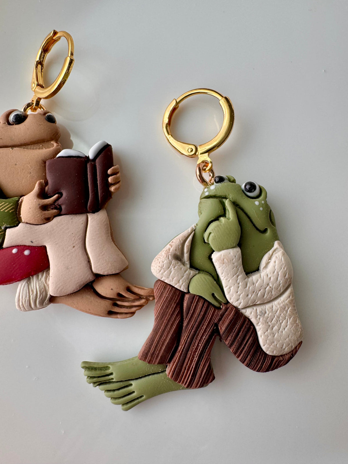 Frog character keychain with gold ring, green face, striped outfit, holding a book