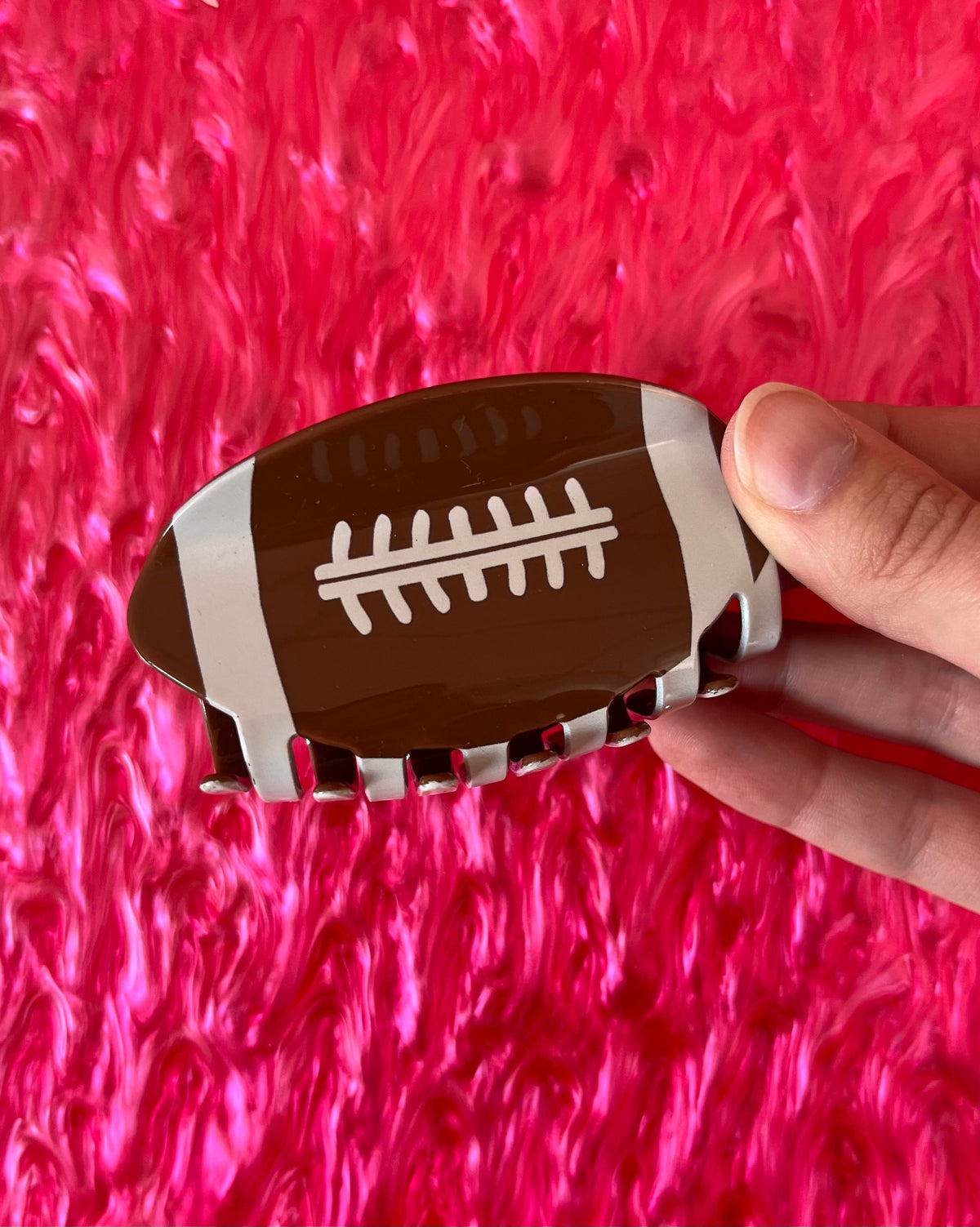 Football-shaped hair claw clip with white stitch lines on dark brown