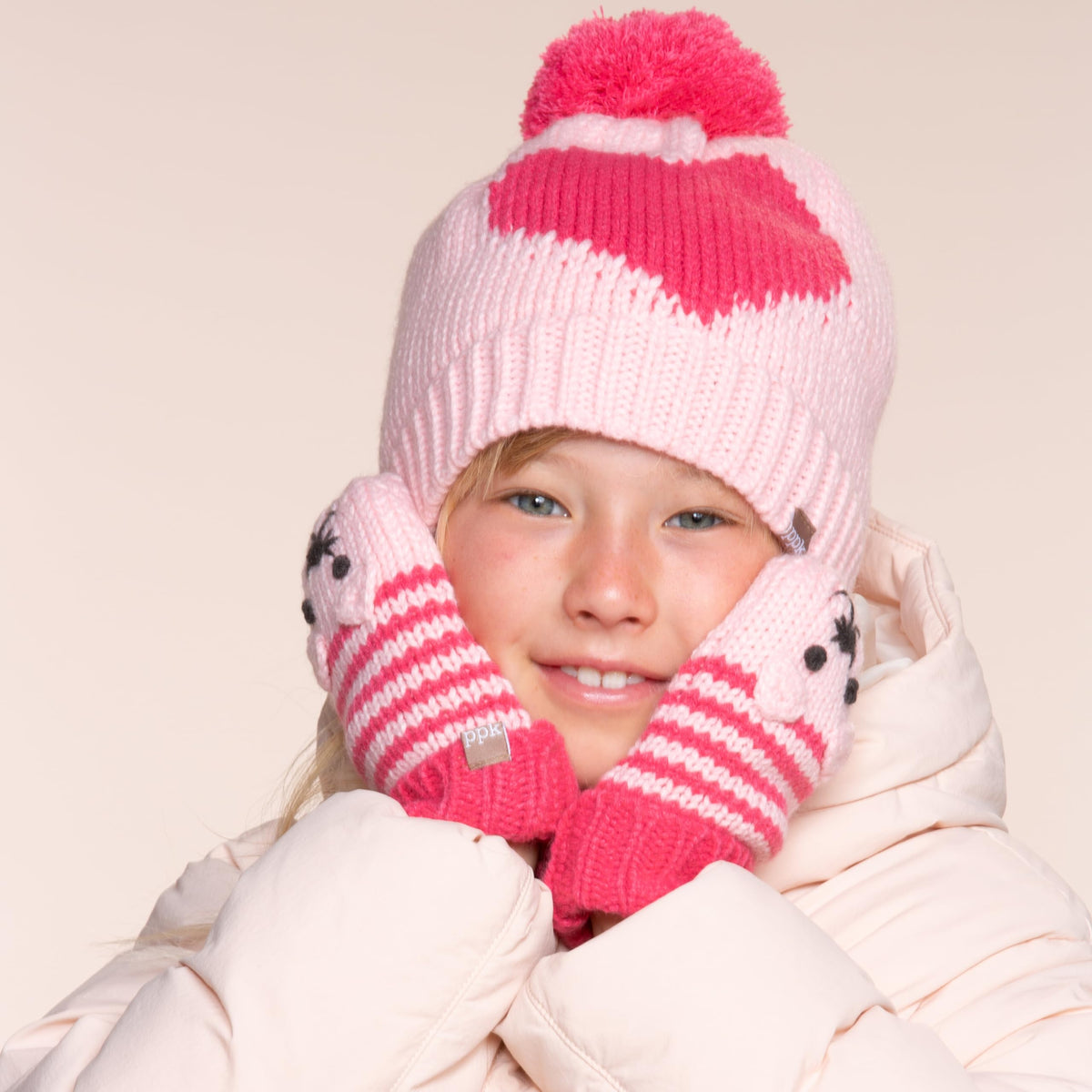 Girl wearing a pink heart-pattern hat and animal mittens with striped cuffs