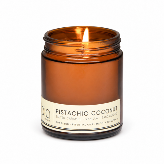 Amber glass candle jar with lid, lit wick, Pistachio Coconut label