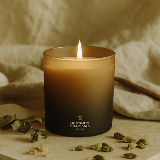 Burning scented candle in amber glass jar with black base and Deandra Craigman logo