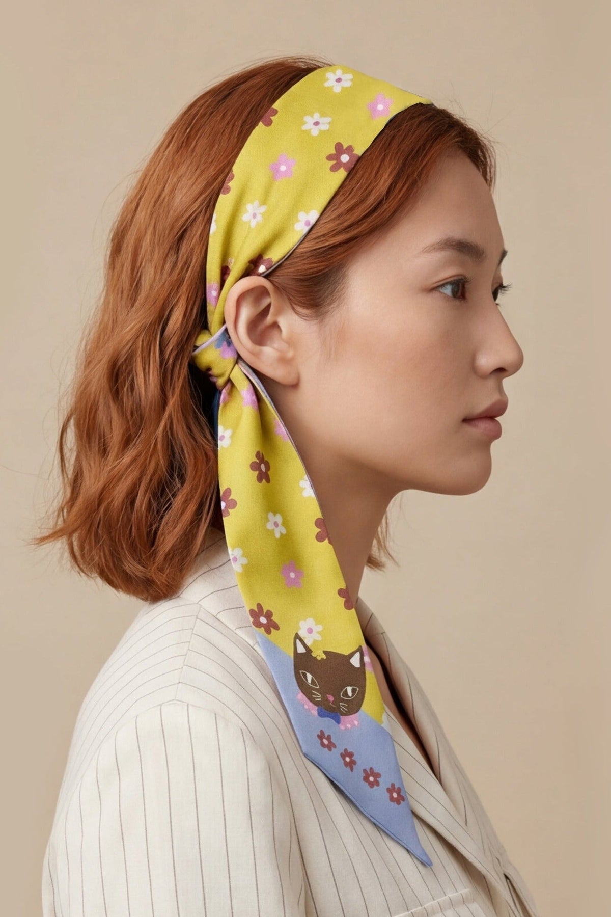 Twilly scarf tied in hair, yellow base with cat and flower prints and blue border