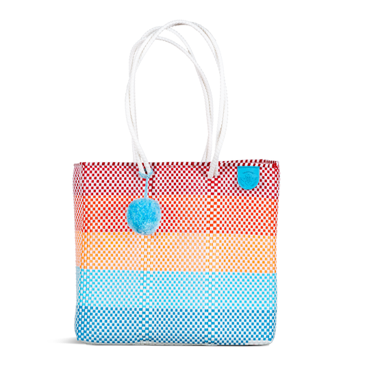 Woven tote bag with red-and-blue check pattern, long white handles, pom-pom charm