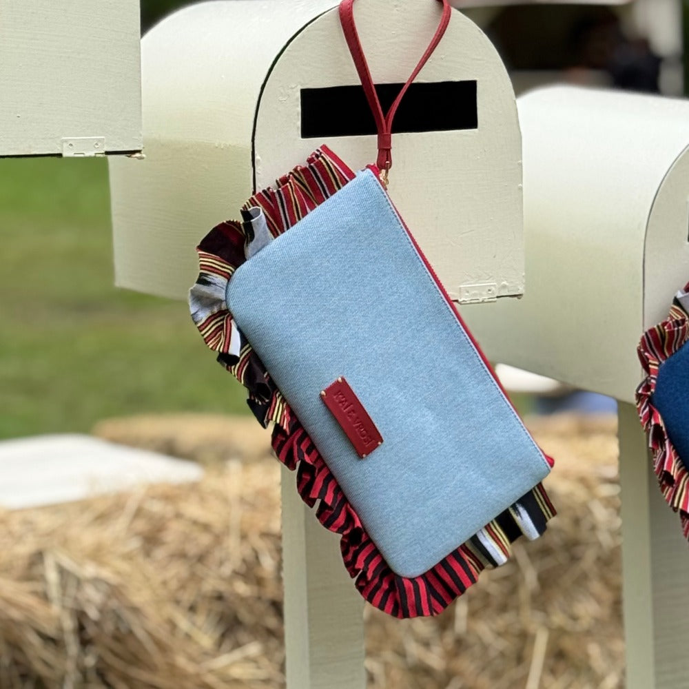 Light blue denim crossbody clutch bag with fringed striped strap and red leather patch