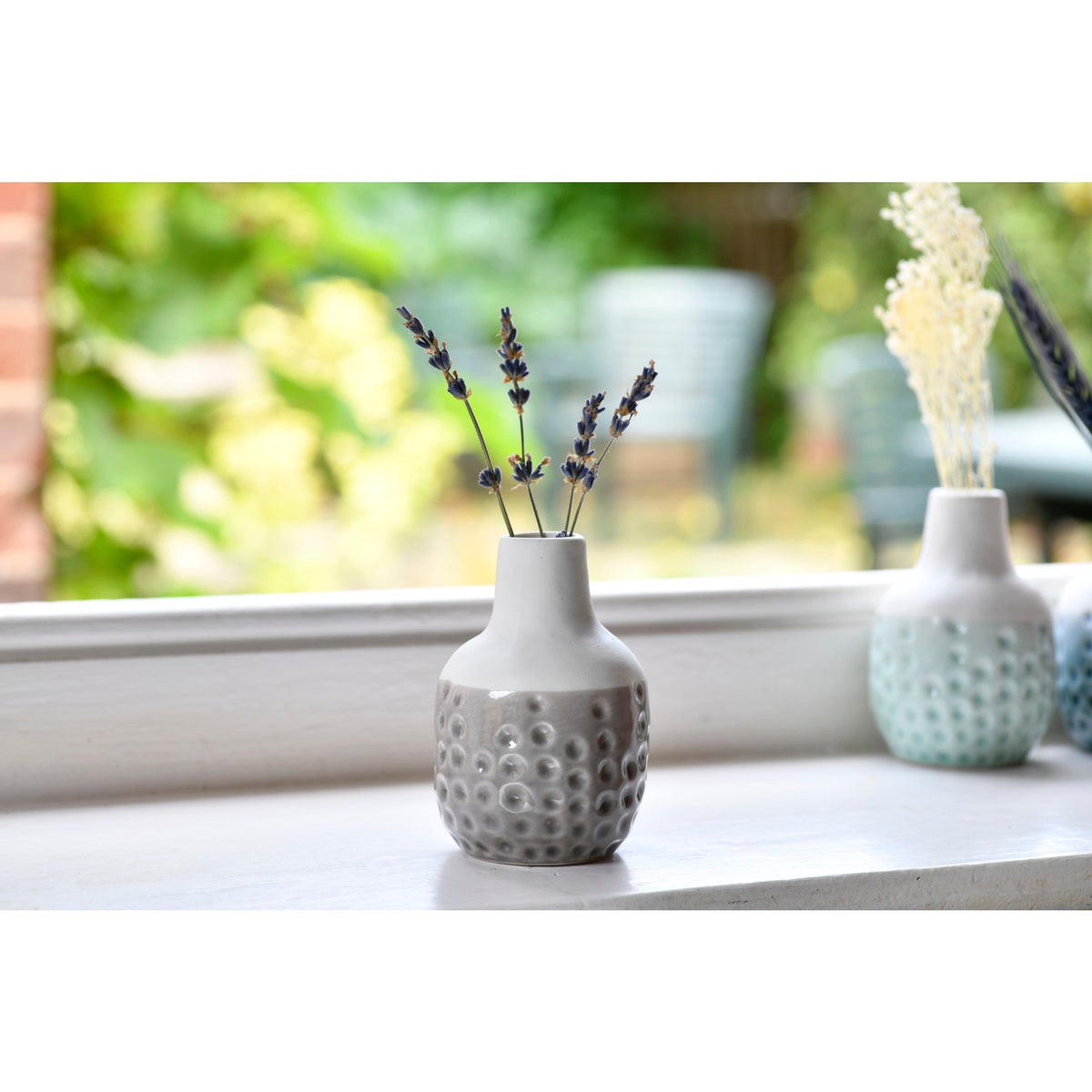 Mini ceramic dot vase with dark flower stems, gray speckled body on windowsill