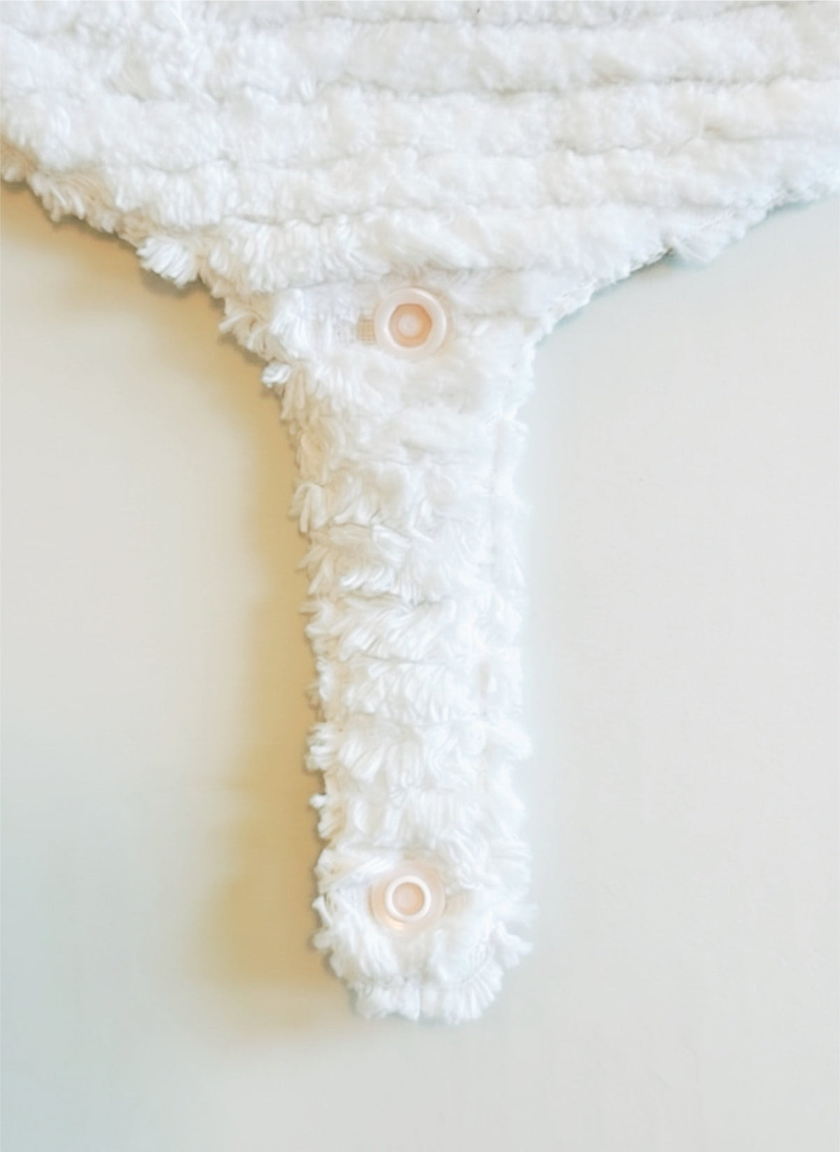 Close-up of white fuzzy pacifier bib with round snap detail