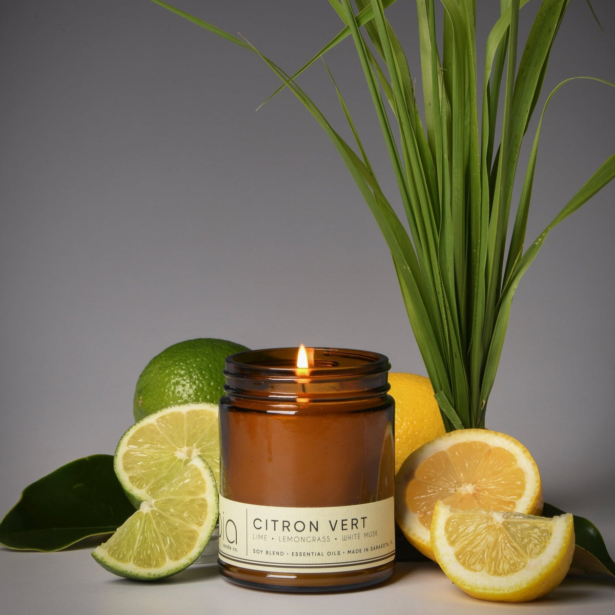 Amber soy blend candle with lit wick and Citron Vert label, surrounded by citrus halves.