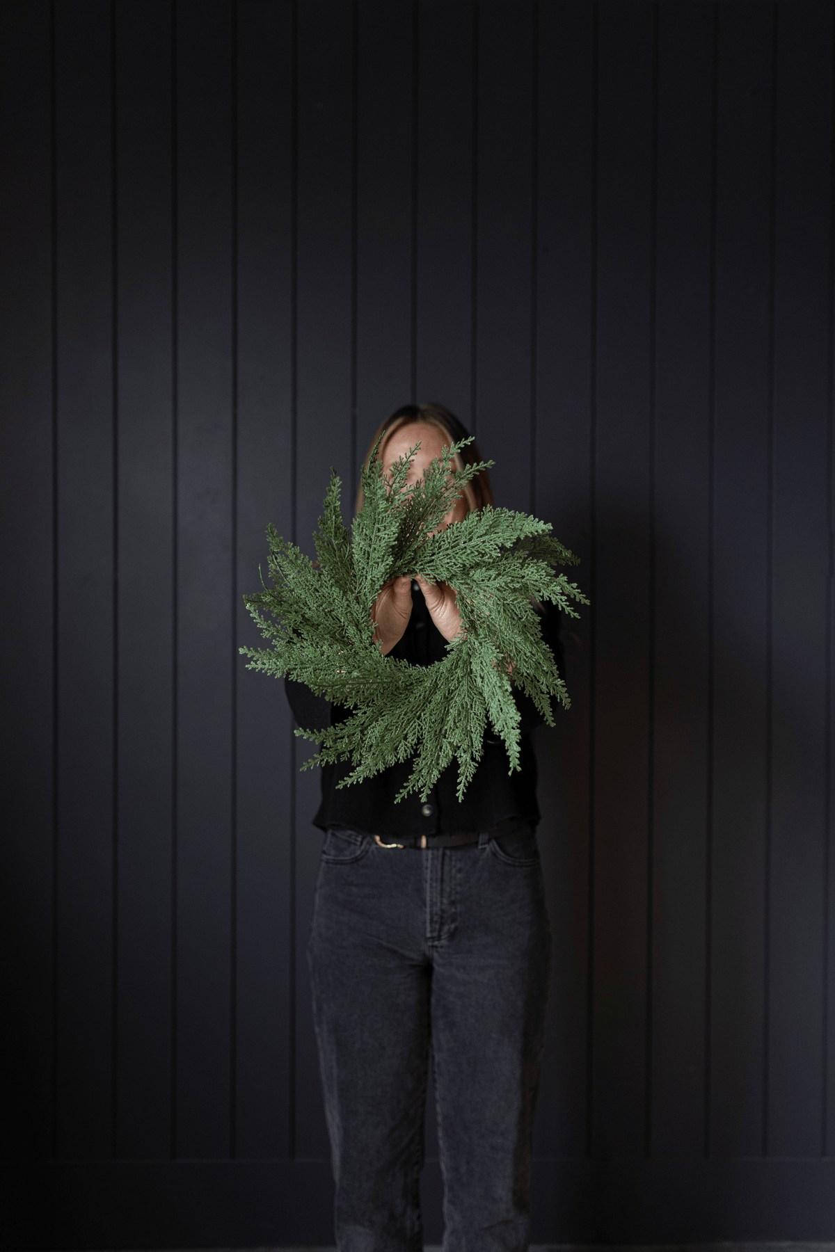 Green cypress leaf wreath held up by hands, showing full foliage