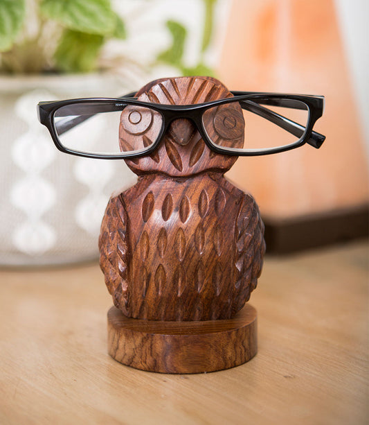 Hand-carved wooden owl eyeglass holder with black eyeglass frames across the face.
