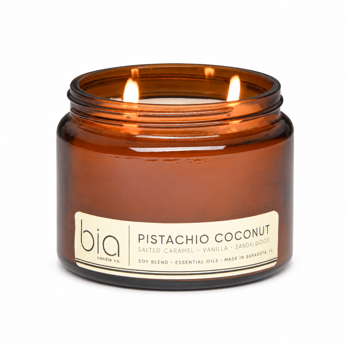 Amber glass candle jar with lit wicks, “Pistachio Coconut” label