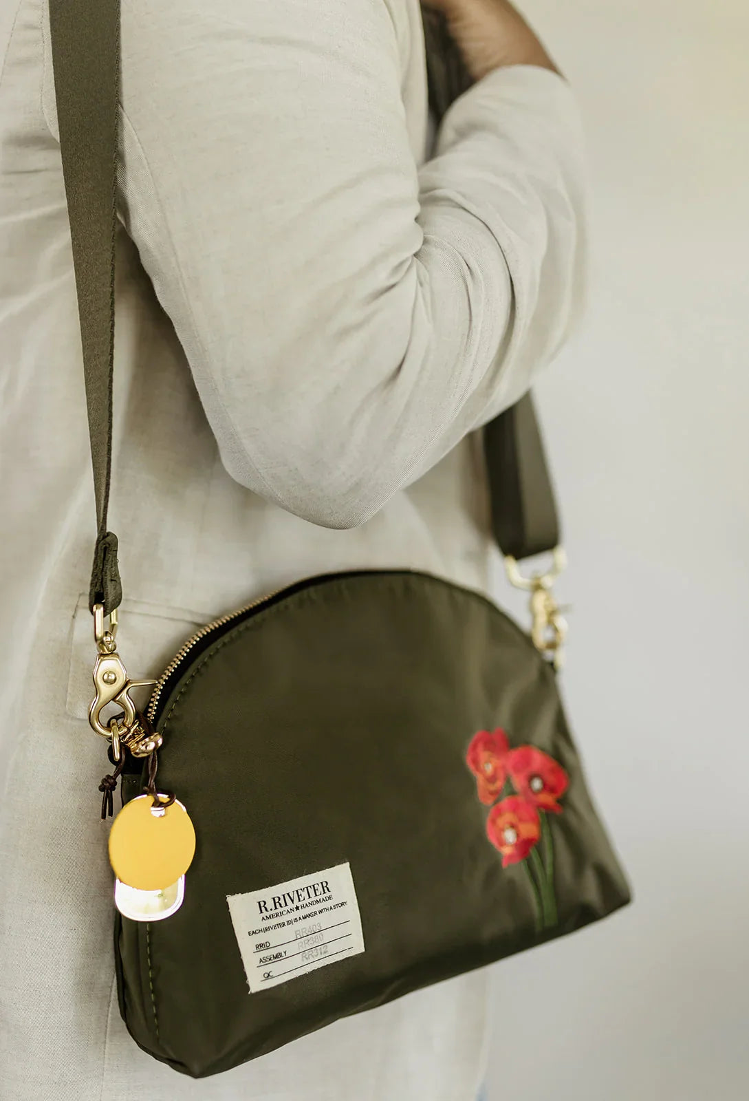 Olive nylon crossbody bag worn, with red poppy embroidery, strap, and zipper top