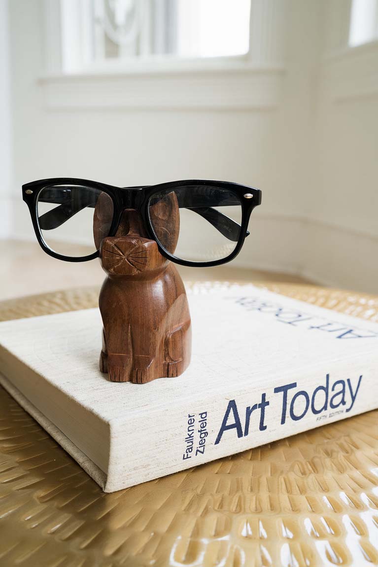 Hand-carved wooden cat eyeglass stand with black glasses resting on its head