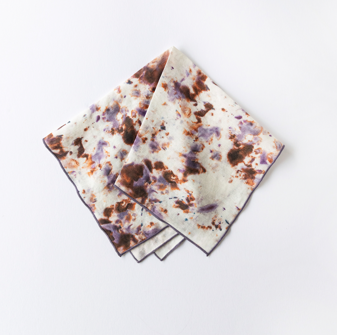 Two marble-pattern napkins folded together, white with multicolor splatter and plum trim.