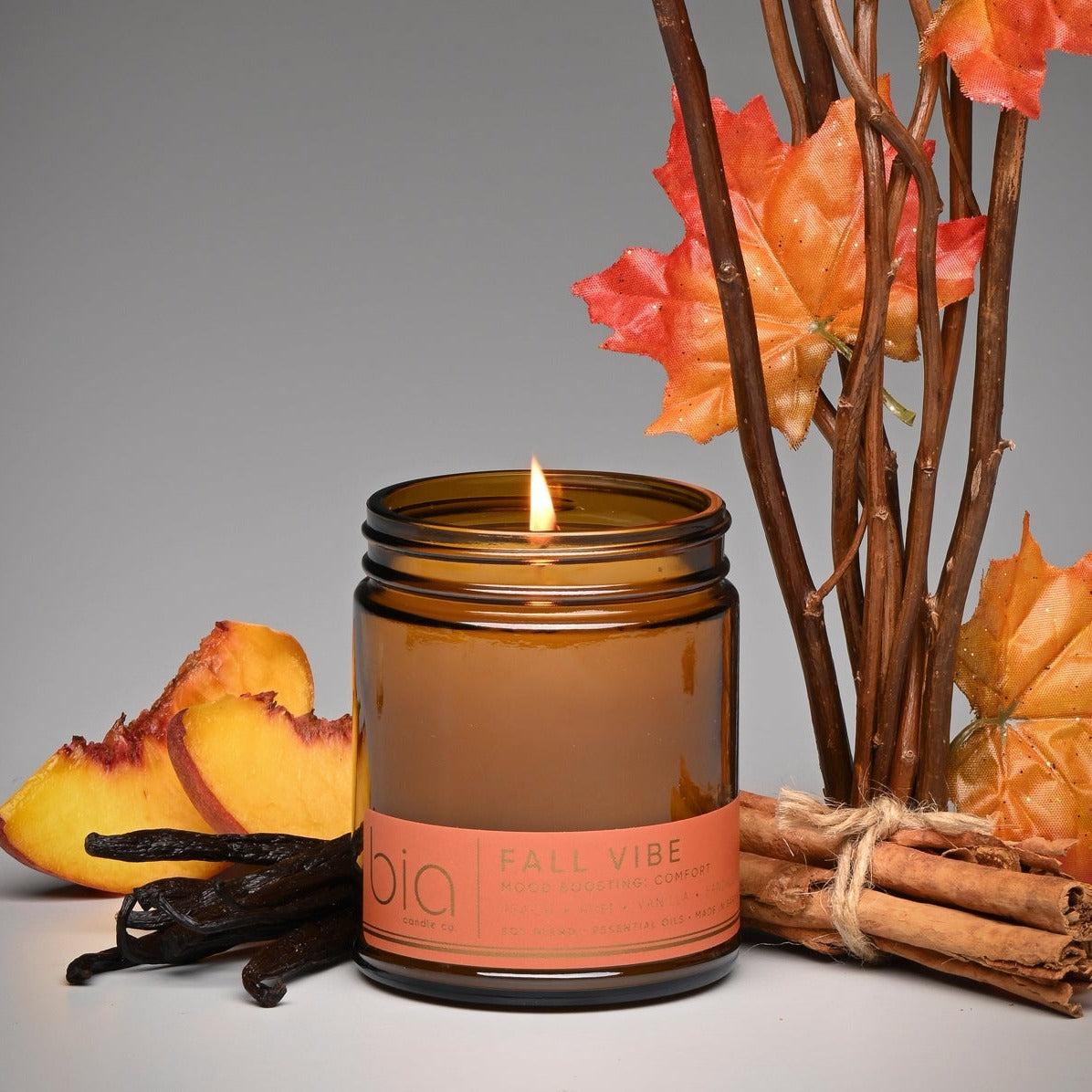 Amber glass soy blend candle with lit wick and 'bio' label, with autumn leaves