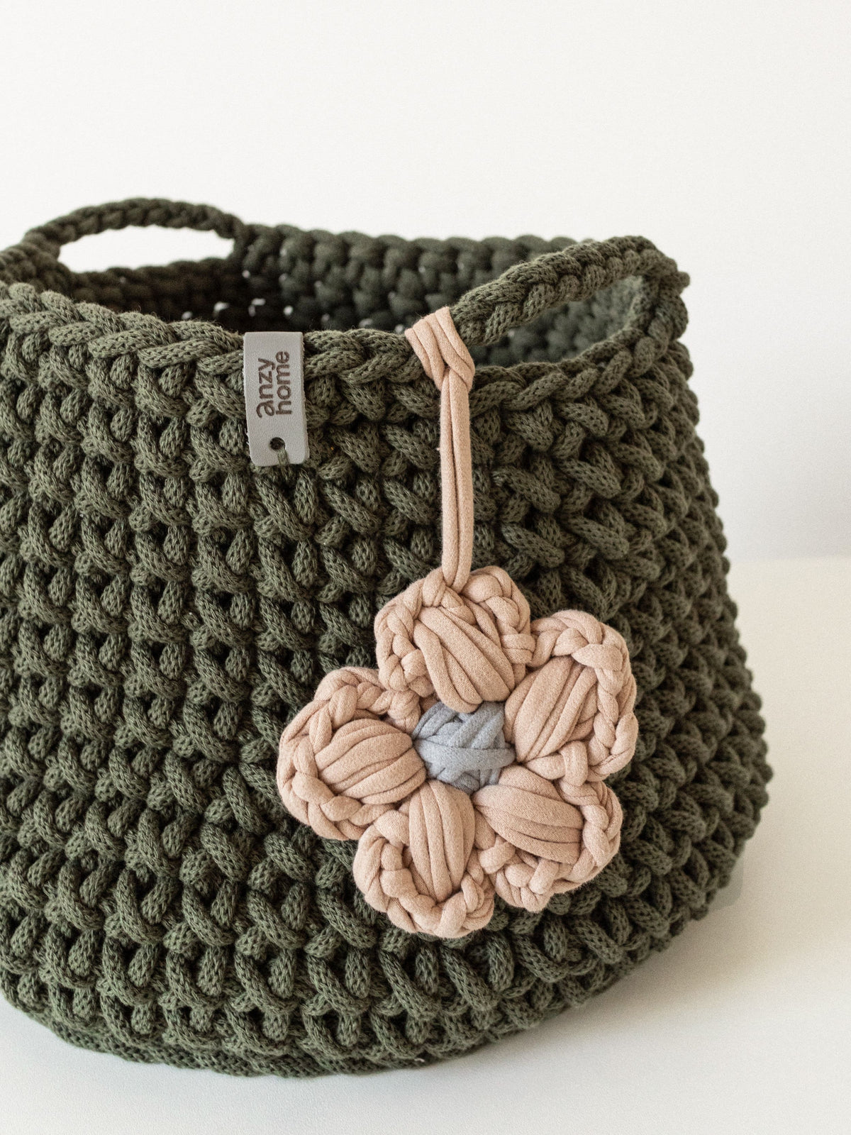 Close-up of olive green crochet storage basket with pink and blue flower detail