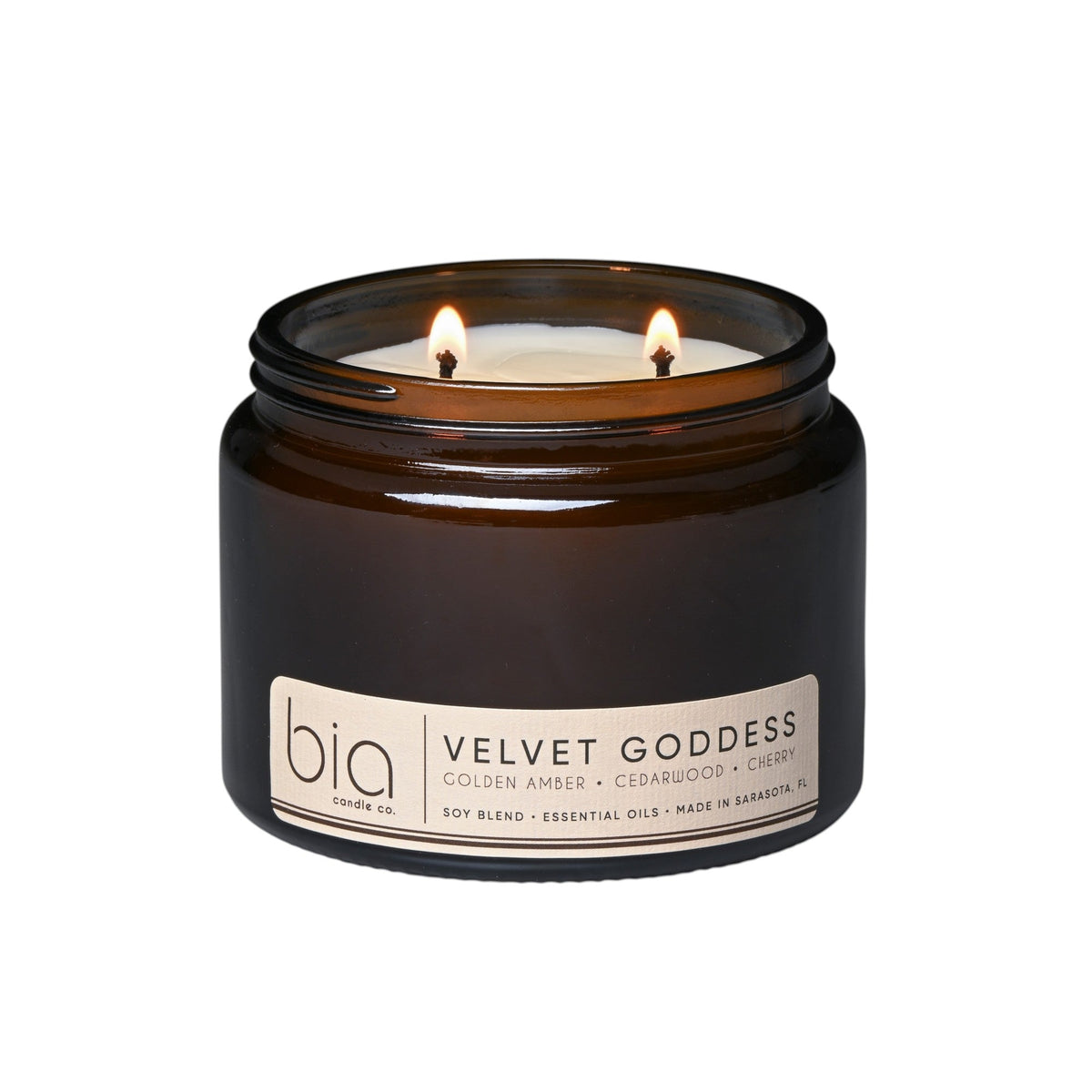 Dark brown glass soy candle jar with two lit wicks on a white background