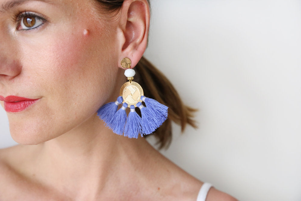 Blue tassel drop earrings worn with gold disc and white bead accents on ear