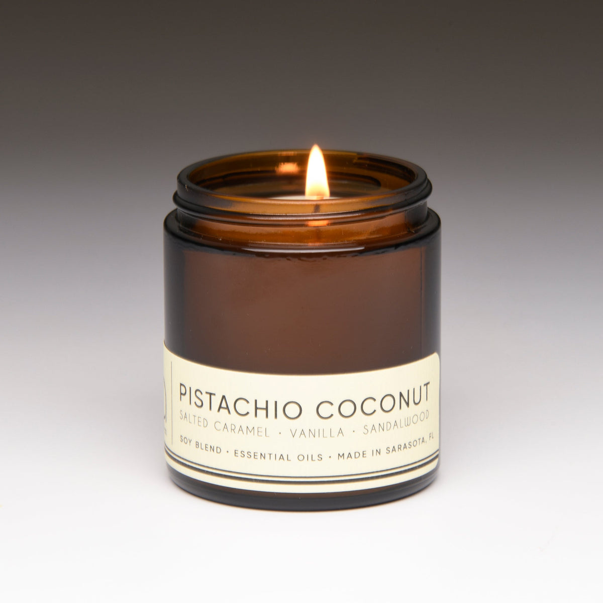 Amber glass candle jar with a lit wick and “Pistachio Coconut” label
