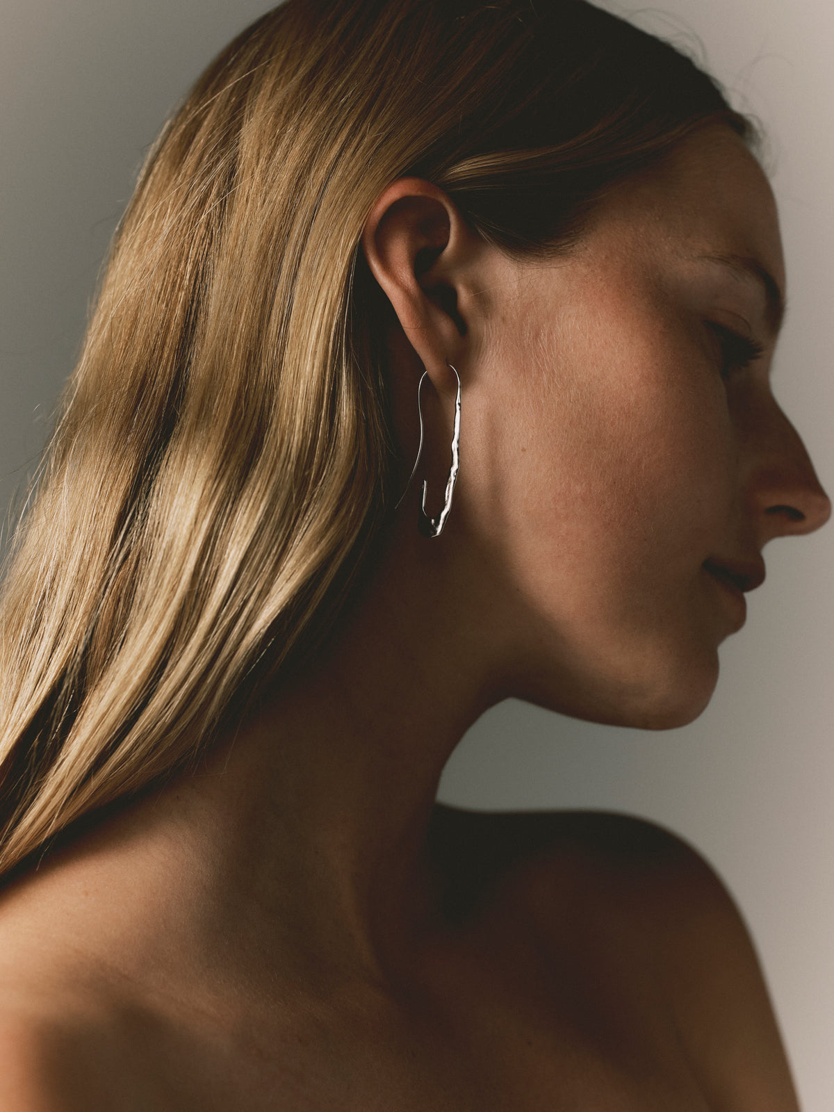 Silver paperclip hoop earrings on ear, elongated wavy link drop