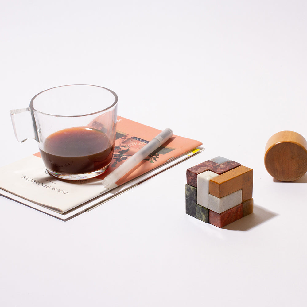 Gemstone cube puzzle with multicolor stone blocks on a tabletop with tea accessories.