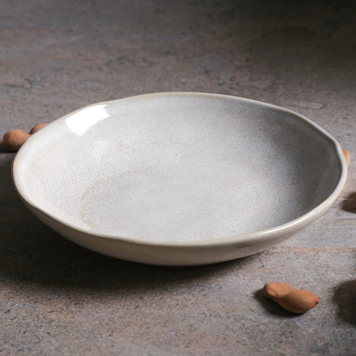 Speckled ceramic pasta plate with shallow bowl and flared rim, light stone color.