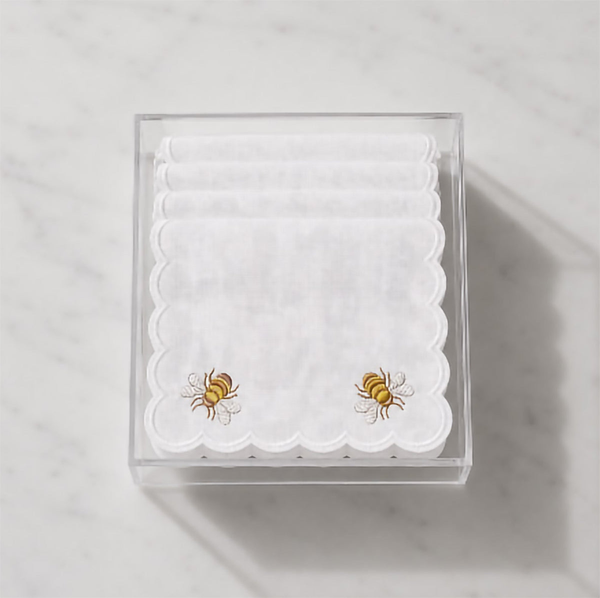 Clear box with folded white cocktail napkins, scalloped edges, honey bee embroidery