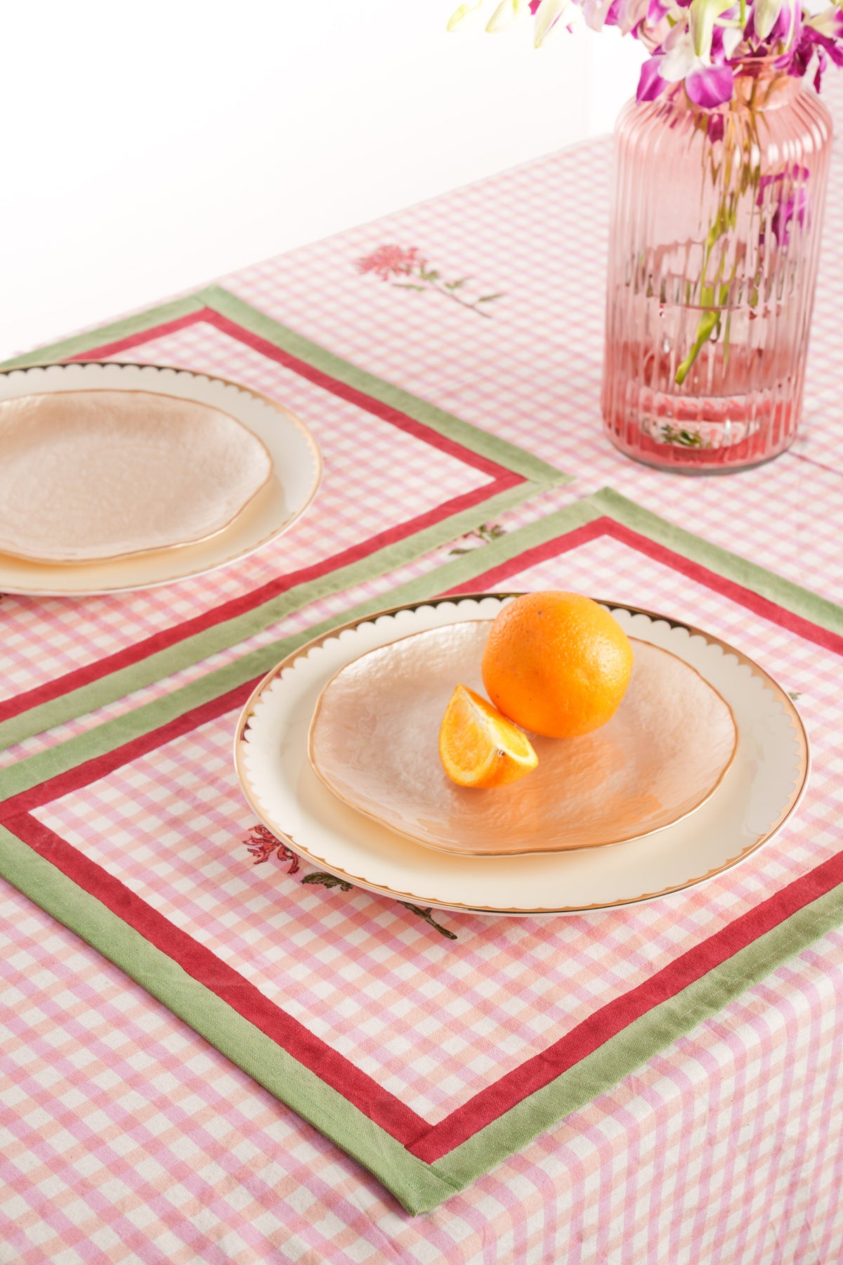 Pink gingham placemat with red floral border and green trim; plate and orange on top
