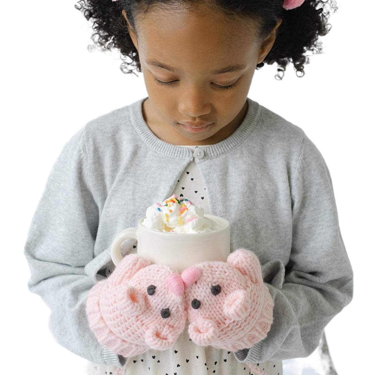 Pink mouse-face knit mittens worn by a child holding a cup