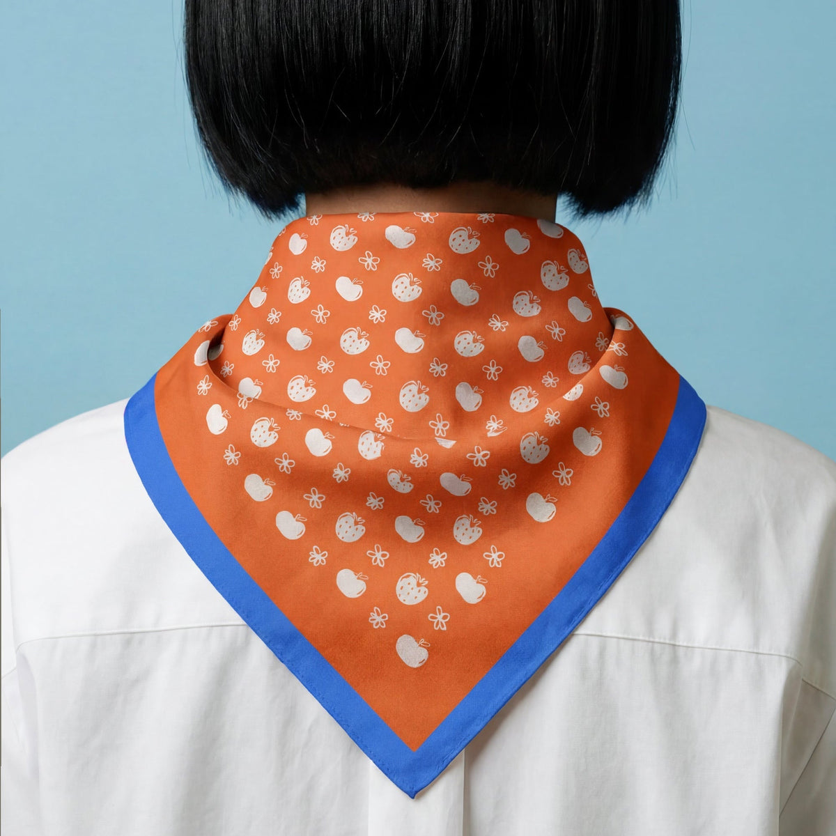 Orange cotton bandana around neck with blue edge and white tiny fruit print.