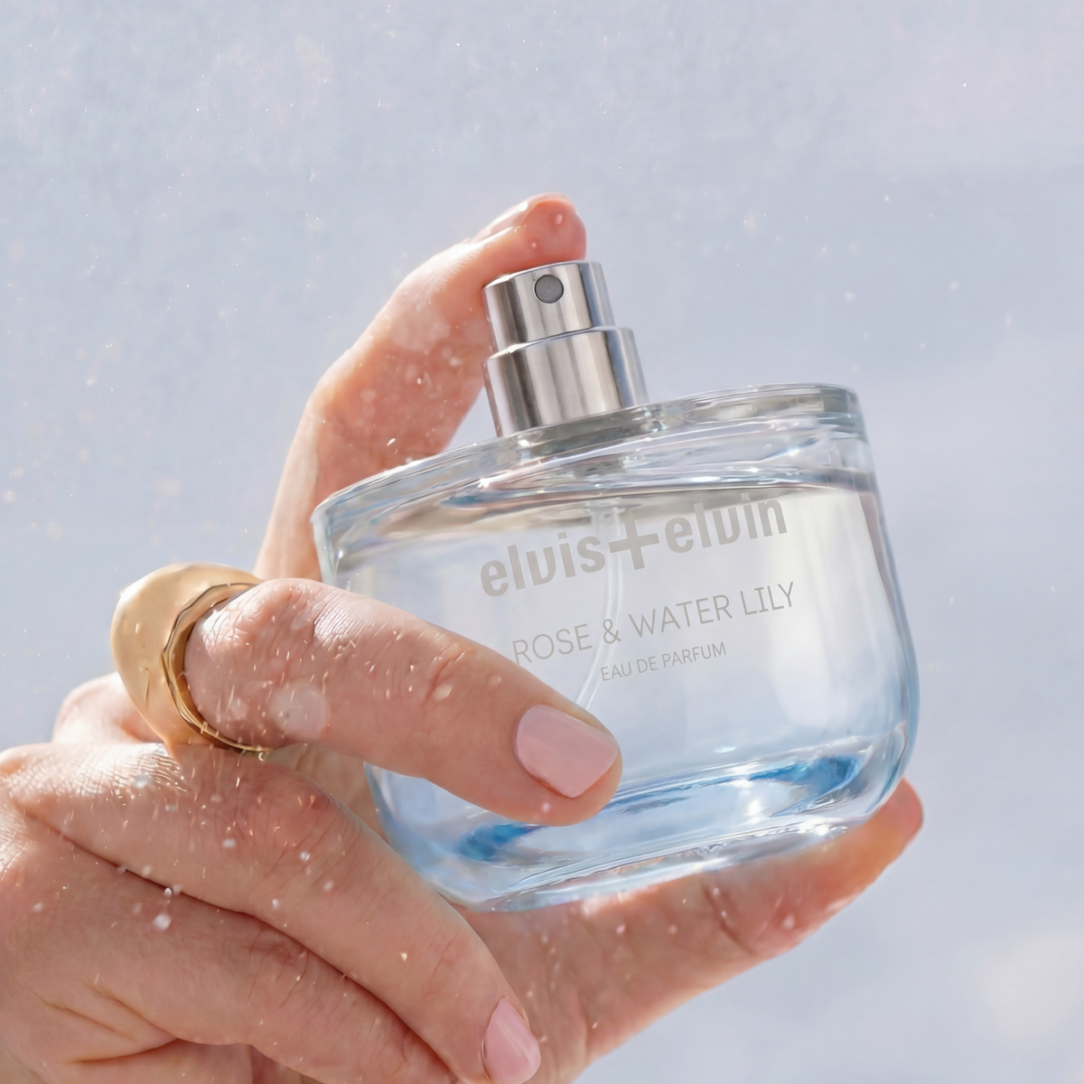 Rose & Water Lily eau de parfum bottle held in hands, mist sprayer visible
