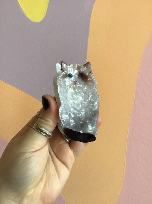 Cat hair claw with silver-toned face and blue eyes, held in hand