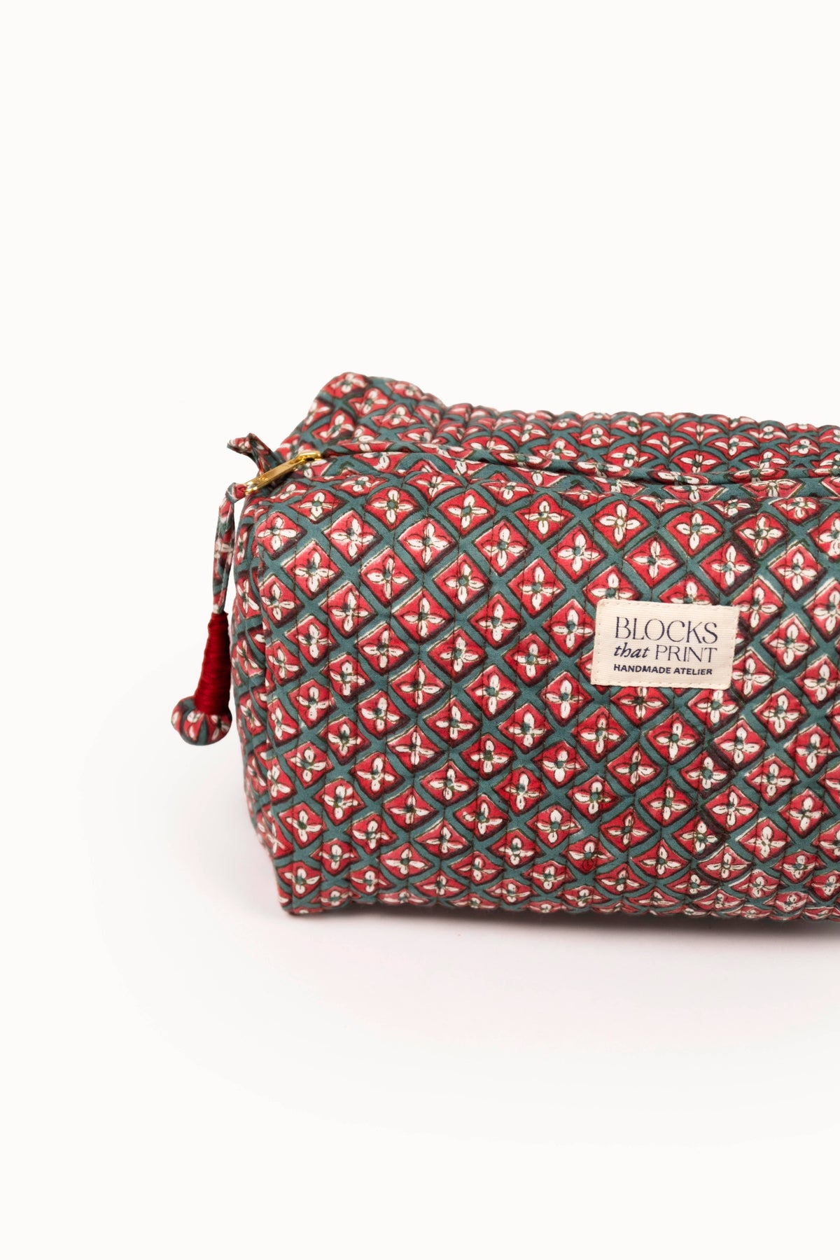 Quilted travel pouch with red and green diamond block print, top zipper and logo patch