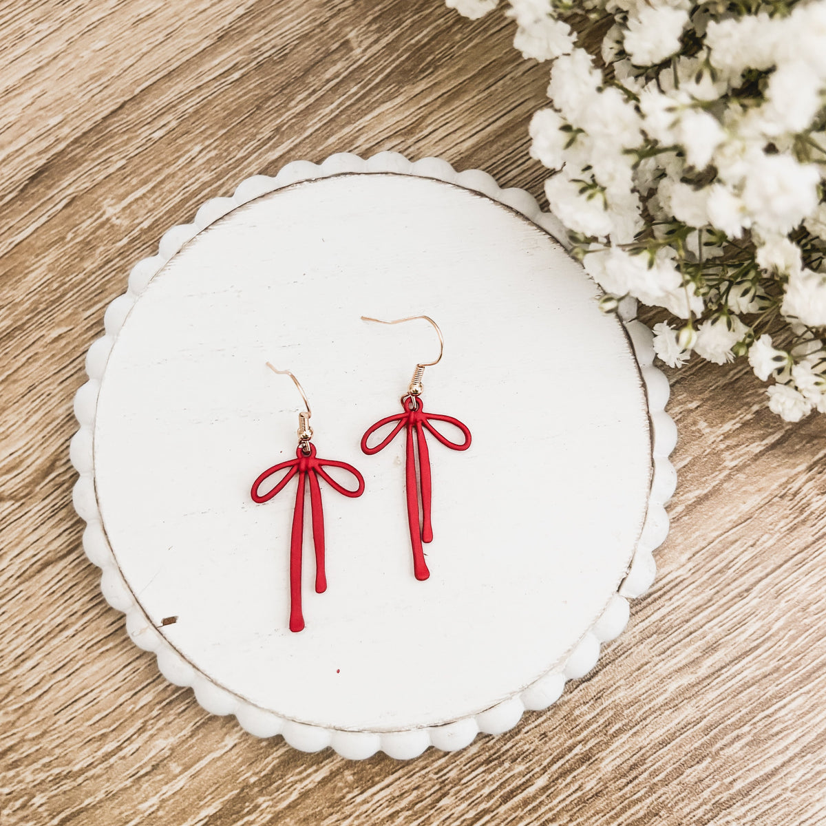 Red bow drop earrings with tassel strands and gold-tone hooks on a white round card
