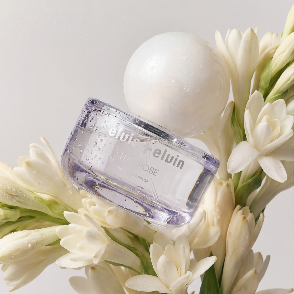 Tuberose eau de parfum bottle angled with white cap among tuberose flowers
