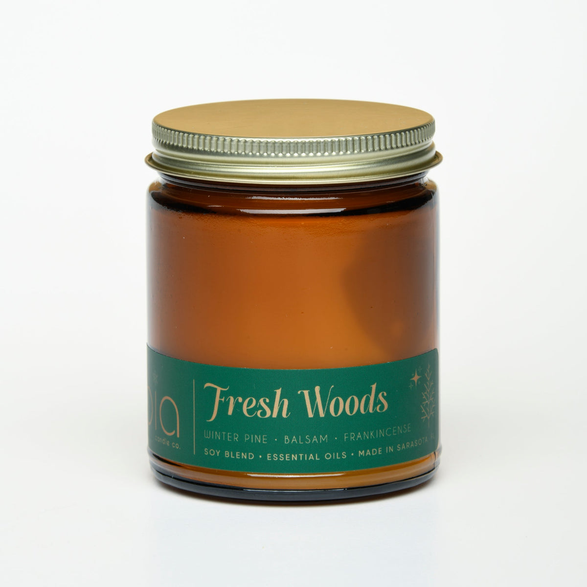 Amber glass candle jar with green Fresh Woods label and gold metal lid, unlit