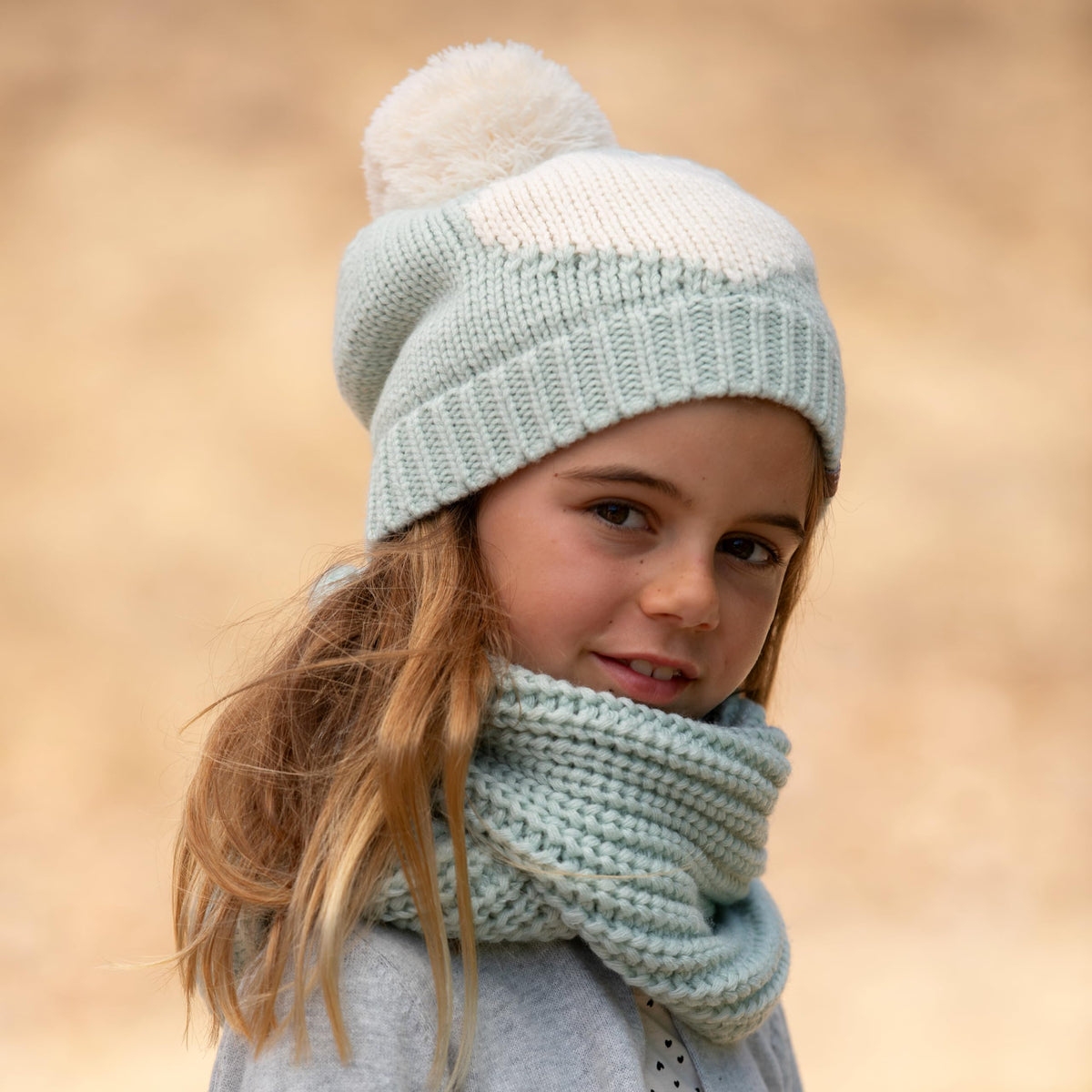 Girl wearing a mint green knitted pom-pom hat and matching scarf