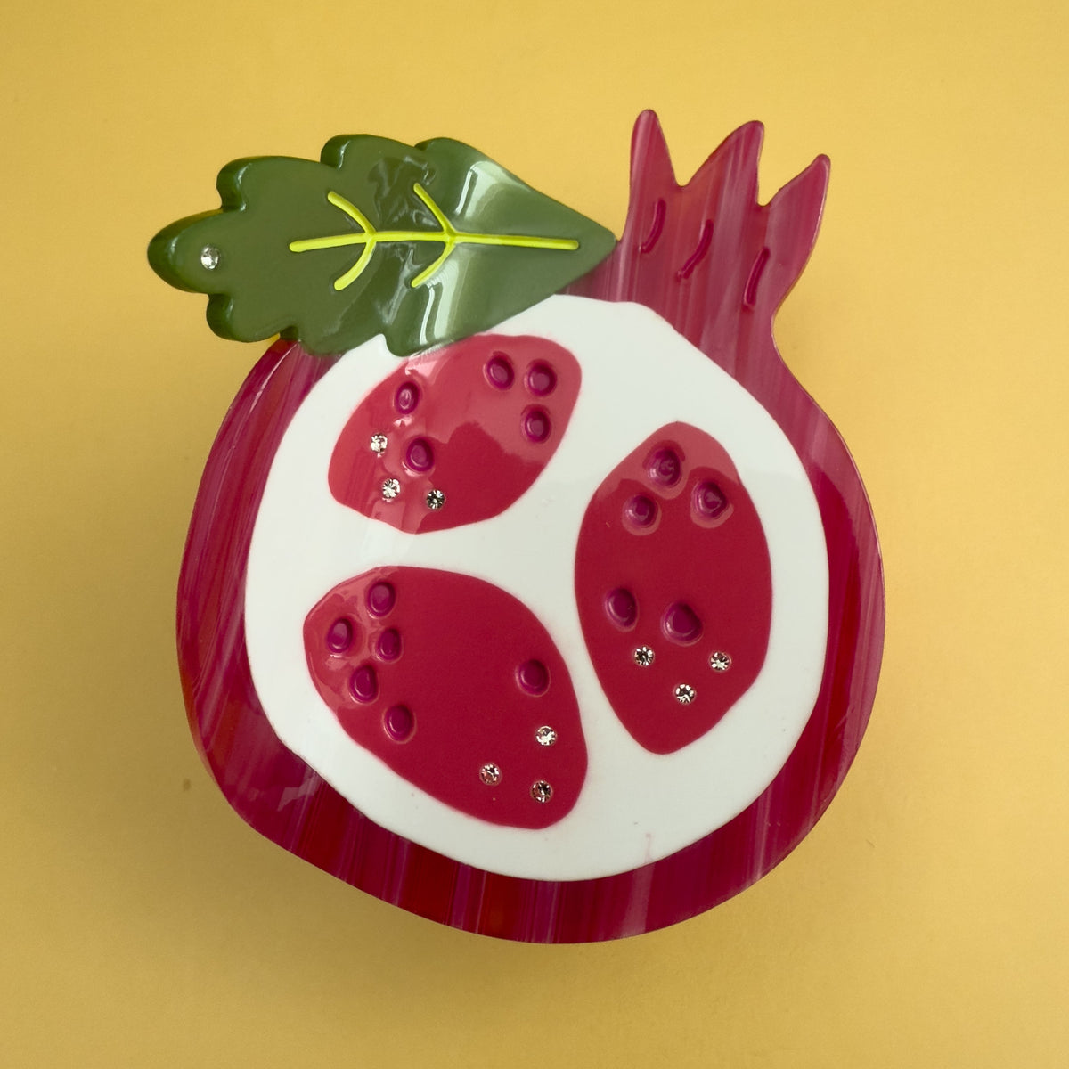 Pomegranate-themed hair claw with red and green leaves, white oval base, rhinestone details