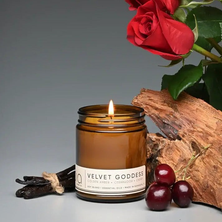 Lit amber glass candle jar on wood with red roses and small berries