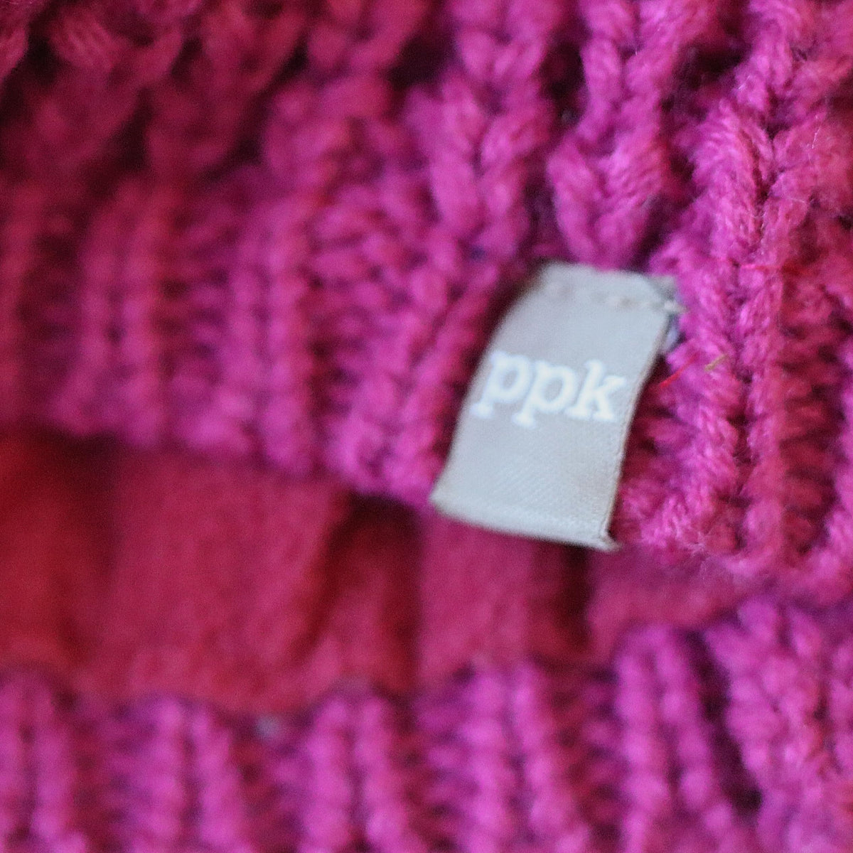 Plum knit beanie close-up showing textured stitches and brand label